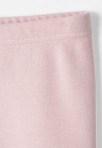 Tela rosa claro con una superficie suave y texturizada; presenta una cintura elástica estrecha con costuras visibles a lo largo del borde superior.