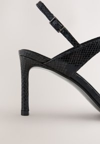 Sandale cu toc înalt, negre, dintr-un material texturat cu model de șarpe, cu o curea subțire la gleznă prevăzută cu o cataramă și toc stiletto ascuțit.