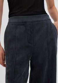 Pantaloni in corduroy grigio scuro con una superficie testurizzata, caratterizzati da una cintura elastica ampia, tasche laterali e cuciture lisce per il comfort.