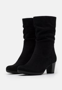 Bottes chelsea en daim noir avec un design fléchi et un talon de 5 cm. Texture lisse avec des détails de couture subtils. Semelles en caoutchouc plates pour une meilleure adhérence.