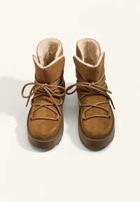 Rjave semiš škornji z mehkimi umetnimi krznom obloženimi notranjosti, zaobljenim prstom in nastavljivim vezanjem. Imajo debel gumijast podplat za boljšo oprijemljivost.