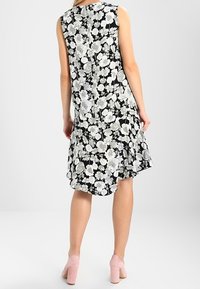 Černé květinové bezramínkové šaty s jemným šedobílým květinovým vzorem, s rozšířeným spodním lemem a diskrétním zadním skladem.