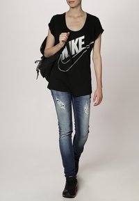 Svart bomull T-shirt med stor grå "NIKE" logotyp, i kombination med ljusblå slitna skinny jeans och svarta sneakers. Ryggsäck på axeln.