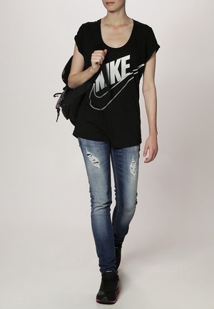 Černé bavlněné tričko s velkým šedým logem "NIKE", spárované se světle modrými zničenými skinny džíny a černými teniskami. Batoh na rameni.