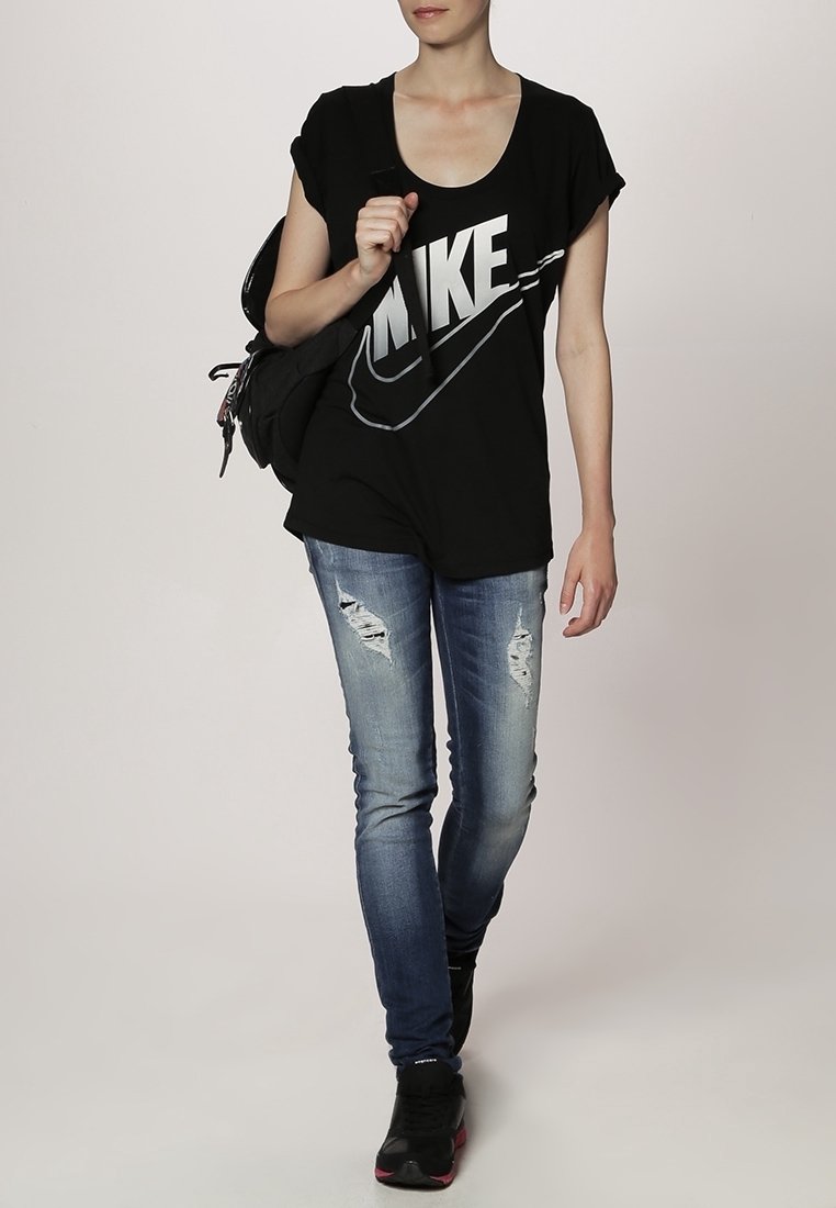 Svart bomull T-shirt med stor grå "NIKE" logotyp, i kombination med ljusblå slitna skinny jeans och svarta sneakers. Ryggsäck på axeln.