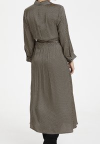 Lång klänning med svart och vitt prickmönster, gjord av mjukt tyg. Har en krage och midja med bälte, samt långa, svävande ärmar.