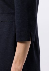 Dunkelblaues Kleid mit einem taillierten Ärmel und einem Schlitzdetail am Bündchen, aus einem strukturierten Stoff gefertigt. Einfaches, minimalistisches Design.