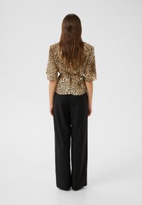 Animal-print blouse in beige and brown with short sleeves, fitted waist, tied at the back, paired with black wide-leg pants.