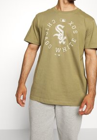 Olivově zelené bavlněné tričko s kulatým výstřihem a krátkými rukávy. Obsahuje bílý kruhový znak s nápisem "Chicago White Sox".