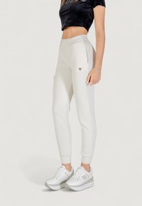 Pantaloni jogger bianchi, aderenti, realizzati in tessuto morbido, con tasche laterali e un piccolo logo sulla fascia in vita. Abbinati a sneakers bianche con suola platform.