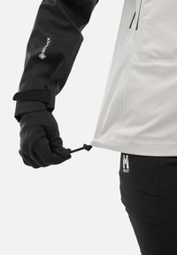 Schwarze und graue GORE-TEX-Jacke mit elastischem Kordelzug am Saum, kombiniert mit schwarzen Handschuhen, mit Logo am Bund.