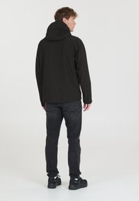 Black hooded jacket with a smooth exterior, paired with dark gray slim-fit jeans and sturdy black sneakers. Simple, functional design.