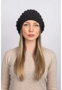 Gorro de lana negro de punto con un diseño texturizado y acanalado. Material de lana suave. El modelo lleva un suéter beige claro, que contrasta con el gorro.