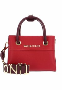 Red Valentino -laukkussa on tumma ruskea kahva, kultainen logo ja irrotettava hihna, jossa on suurilla kultaisilla kirjainyhdistelmillä kirjoitettu "VALENTINO."