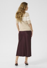 Suéter de punto beige con rayas blancas en los hombros, combinado con una larga falda de satén burdeos. Modelo de espaldas vistiendo tacones negros.