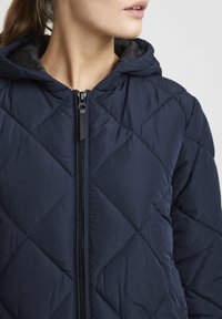 Navy quilted puffer jacket with a hood, featuring a front black zipper, and diamond-shaped stitch pattern. Smooth fabric texture.