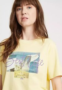 Żółta bawełniana koszulka z krótkim rękawem z graficznym nadrukiem przedstawiającym scenę plażową oraz napisem "Best Life" w kolorze fioletowym. Luźny krój.