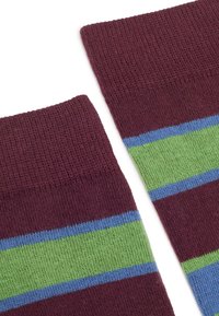 Primo piano di calzini a maglia color bordeaux con strisce orizzontali verdi e blu vicino alla parte superiore su uno sfondo bianco.