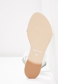 Sandale blanche avec une semelle lisse et plate. Dispose d'une bride à la cheville unique avec une garniture argentée. Estampillée "MADE IN ITALY" et taille 37.