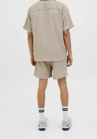Beige gestreept shirt met korte mouwen en bijpassende korte broek, gemaakt van lichtgewicht stof, gecombineerd met grijze sneakers en witte sokken met zwarte strepen.