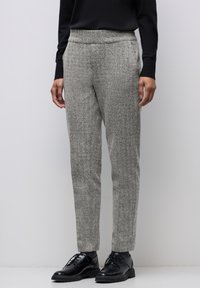 Pantalons texturés gris en laine, avec une coupe ajustée, une taille élastique et des poches latérales, associés à des chaussures noires à lacets.