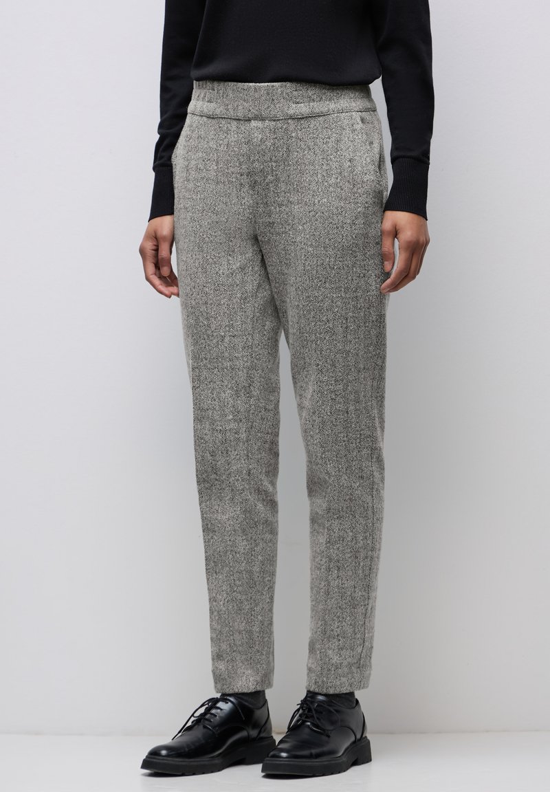 Pantalons texturés gris en laine, avec une coupe ajustée, une taille élastique et des poches latérales, associés à des chaussures noires à lacets.