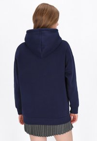 Sudadera con capucha azul marino, mangas largas, puños acanalados y un ajuste relajado. La tela parece suave con una textura lisa.
