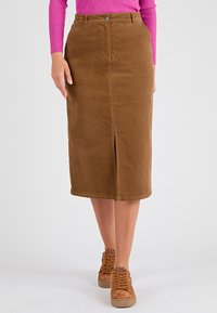 Falda midi de pana marrón con abertura frontal, cierre de botón metálico y trabillas para cinturón. Combinada con zapatillas beige que presentan detalles de estampado de leopardo.