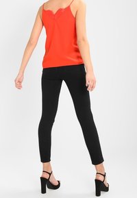 Camiseta roja sin mangas con encaje, combinada con jeans negros ajustados y sandalias de tacón alto negras. Vista posterior, tejido suave, silueta esbelta.