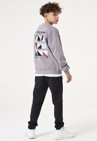 Grijze sweatshirt met een geometrische print op de rug, gecombineerd met donkere broeken en witte sneakers. Casual pasvorm, ontspannen stijl, zachte textuur.