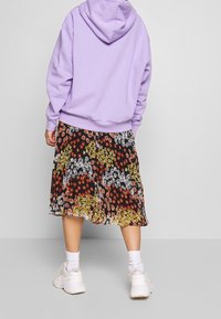 Sudadera con capucha en color lila combinada con una falda negra de flores que presenta flores rojas, amarillas y blancas. Zapatillas blancas con suelas visibles.