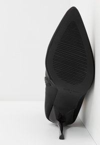 Scarpa nera con tacco alto e punta affilata, upper sintetico elegante e suola nera testurizzata. Presenta un design minimale e una silhouette senza cuciture.