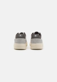 Baskets en suede et tissu gris avec une semelle beige ; elles présentent un logo circulaire au niveau du talon et un col rembourré pour le confort.