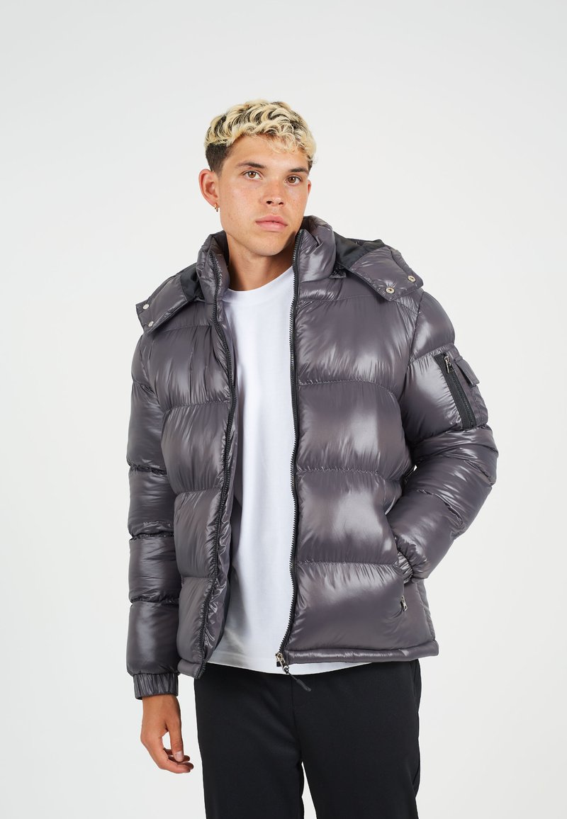 Geïsoleerde jas in metallic grijs met een rits aan de voorkant, afneembare capuchon en elastische manchetten. Voorzien van zijzakken en een ritszak op de arm.