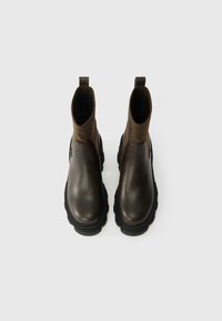 Καφέ δερμάτινες μπότες έως τον αστράγαλο με χοντρές μαύρες καουτσούκ σόλες. Διαθέτουν λεία υφή, στρογγυλή μύτη και θηλιά για εύκολη φόρεμα.