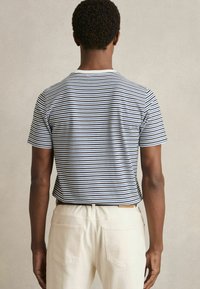 Tricou cu mânecă scurtă în dungi, de culoare albastră și albă, din bumbac, cu guler rotund. Asortat cu pantaloni de culoare crem, cu două buzunare la spate.
