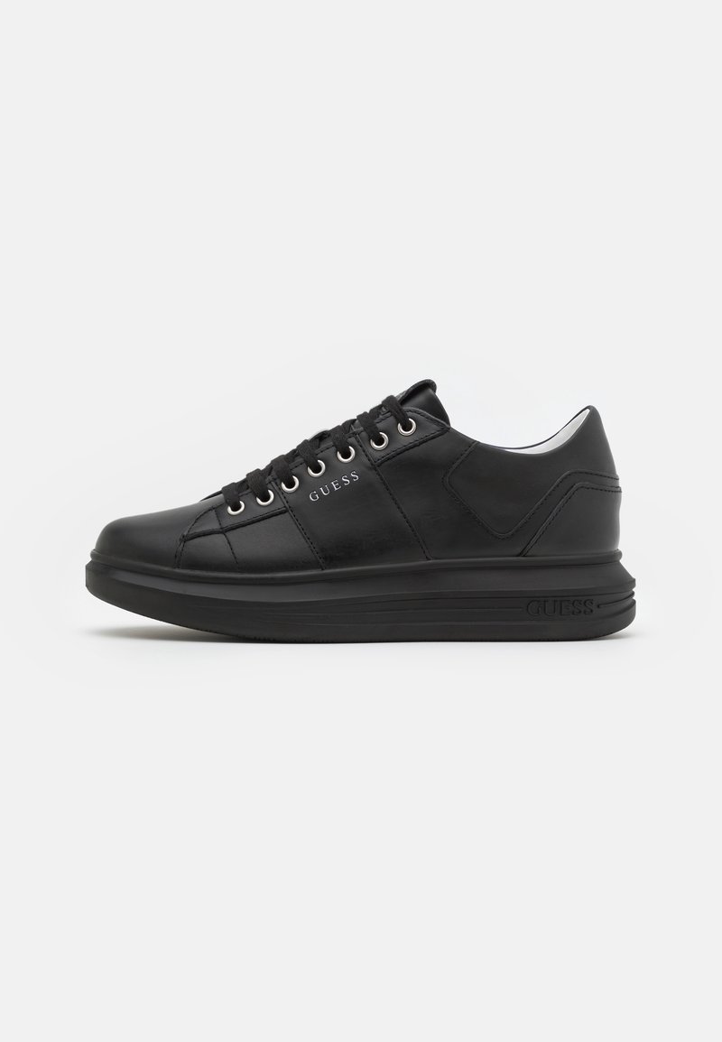 Baskets basses en cuir noir avec lacets, œillets argentés et marquage "GUESS" sur le côté et la semelle, présentées en vue de profil côté droit.