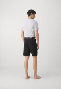 Chemise grise à manches courtes associée à un short noir avec une ceinture élastique à logo. Le modèle est pieds nus, vu de dos.