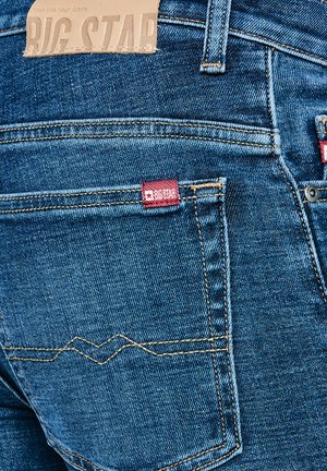 Blå denimjeans med baglomme, der viser gul syning, rød Big Star-mærkat og beige læderlabel ved taljen.