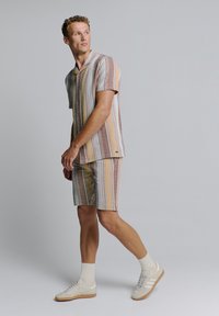 Gestreepte kortek mouwhemd en bijpassende shorts in beige, roest en mosterd tinten. Gemaakt van lichte stof met een knoopsluiting aan de voorkant en een kraag.