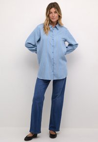 Blue striped oversized button-up shirt with a collar, long sleeves, and blue buttons, paired with dark blue straight-leg jeans and black flats.