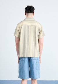 Camicia a maniche corte a righe beige con vestibilità rilassata, abbinata a pantaloni shorts in denim azzurro chiaro lunghezza ginocchio con tasche laterali.