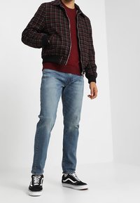 Punainen ja musta ruudullinen bomber-takki, viininpunainen neule, siniset farkut ja mustat tennarit valkoisilla pohjilla. Rennon kerrosvaatetuksen asu.