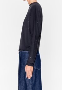 Maglia nera a maniche lunghe con piccole decorazioni colorate, tessuto morbido, vestibilità ampia e scollatura rotonda; abbinata a una gonna di jeans.