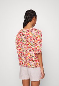 Blusa floral com mangas curtas bufantes, apresentando um padrão vibrante de flores rosas, laranjas e amarelas sobre um fundo claro.