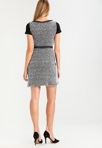 Top corto nero a maniche corte abbinato a un vestito grigio a scacchi houndstooth, caratterizzato da una vita aderente e un orlo frangiato, completato da scarpe nere con tacco alto.