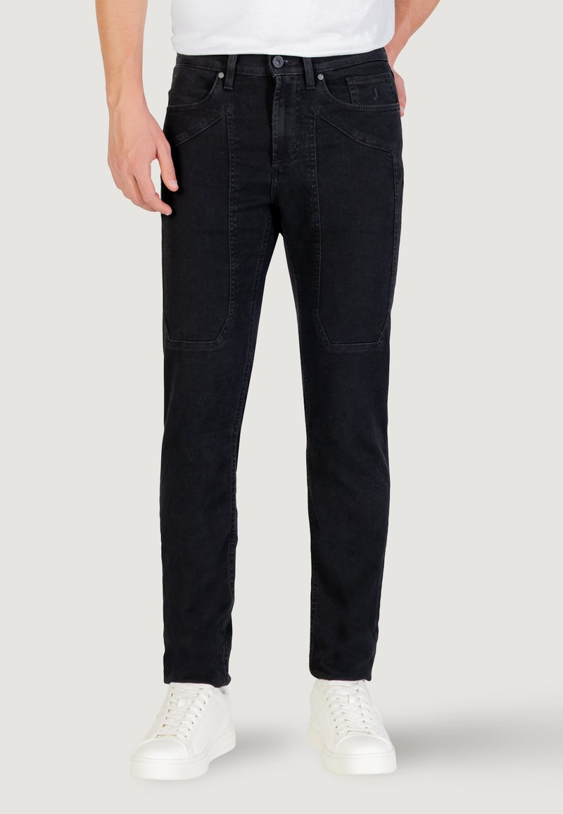 Jean en denim noir slim fit, avec des poches avant, des coutures visibles et une fermeture à bouton, associés à des baskets blanches.