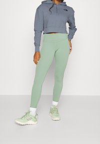 Felpa croppata grigia chiara con logo, leggings a vita alta verde menta e sneakers verde chiaro con accenti e lacci bianchi.