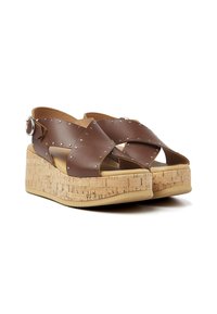Bruine leren wedge sandalen met kruislings ontwerp, zilveren studs, kurken platform en verstelbare enkelband. Textuur oppervlak.