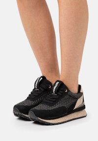 Sneaker nere e strutturate con tomaia intrecciata, dettagli in suede e una suola intermedia beige. Presenta una punta arrotondata e chiusura con lacci.